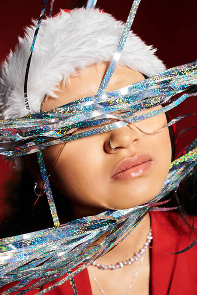 Красивая азиатка обнимает праздничный дух с блестящими лентами, в зимней шляпе.