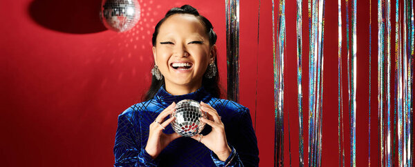 Радостная азиатка наслаждается живым моментом с игристым диско-шаром и ярким декором.