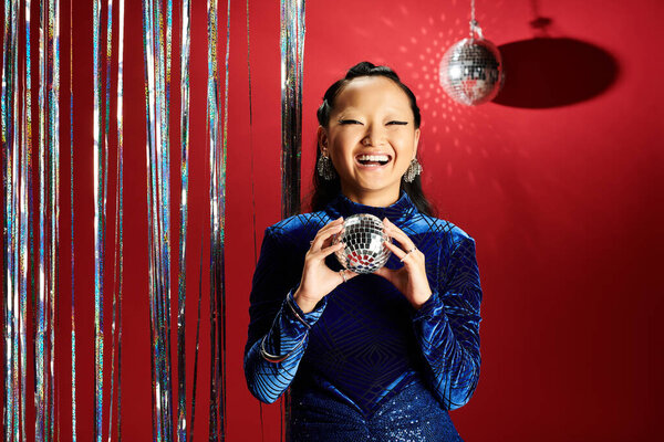 An enthusiastic Asian woman smiles brightly while holding a disco ball, radiating joy.