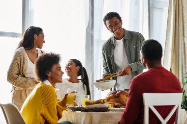 A group of friends celebrates Thanksgiving, enjoying food and laughter in a cozy home setting. clipart