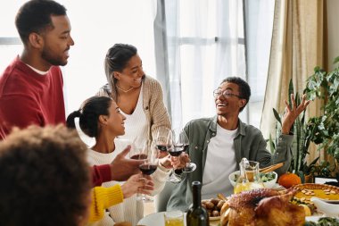 A group of friends shares laughter and drinks during a cheerful Thanksgiving dinner together. clipart