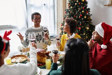Bir grup arkadaş Noel yemeğinin tadını çıkarıyor, gülüyor ve kutlama için kadeh kaldırıyorlar..
