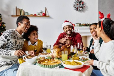 Bir grup arkadaş, Noel 'i evde kutlarken kahkaha ve lezzetli yemekleri paylaşıyor..
