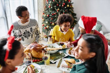 Bir grup arkadaş bir Noel yemeğini paylaşıyor, birlikte yemek, içmek ve kahkaha atıyorlar..