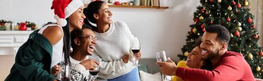 A group of friends shares laughter and drinks in a warmly decorated living room during Christmas. clipart