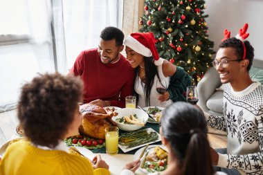 A cheerful gathering of friends sharing a holiday meal and laughter in a cozy living room. clipart