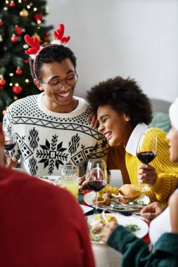 Bir grup arkadaş Noel yemeğinin tadını çıkarıyor, kahkahaları, yemekleri ve iyi arkadaşlıkları paylaşıyorlar..