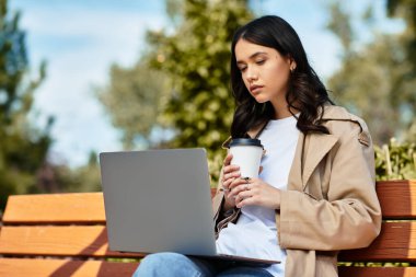 The beautiful young woman in cozy autumn attire is focused on her laptop while sipping a warm drink. clipart