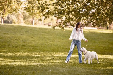 Samimi bir sonbahar kıyafeti giymiş genç bir kadın huzurlu bir park ortamında köpeğiyle oynuyor..