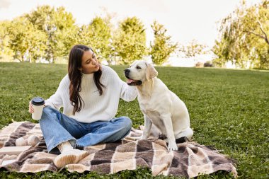 Sıcak sonbahar kıyafetleri içindeki genç bir kadın köpeğiyle battaniyenin üzerinde güzel bir anı paylaşıyor..