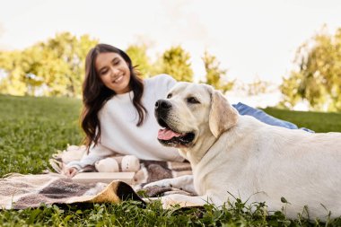 Canlı bir parkta, genç bir kadın sadık köpeğiyle battaniyeye uzanıp mutluluk saçıyor..