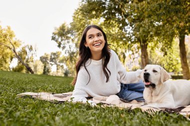 Canlı bir sonbahar parkında, genç bir kadın köpeğini battaniyenin üzerinde kucaklarken neşeyle güler..