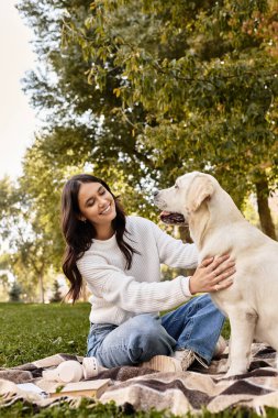 Huzurlu bir parkta, sıcak giysiler içindeki genç bir kadın köpeğiyle sıcak bir battaniyeye sarılmış anın tadını çıkarıyor..
