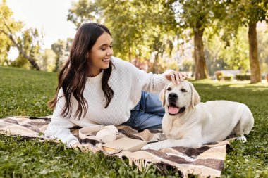 Samimi giyinmiş neşeli bir kadın köpeğiyle oynuyor. Parktaki güneşli sonbahar havasının tadını çıkarıyor..