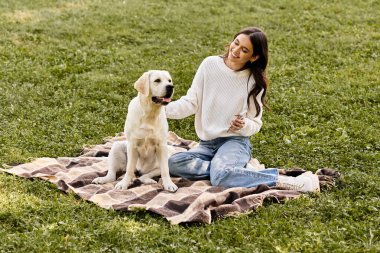 Genç bir kadın, sonbahar yapraklarıyla çevrili rahat bir battaniyede köpeğiyle vakit geçirmekten hoşlanır..