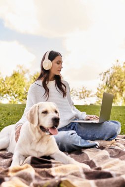Genç bir kadın laptopuyla dışarıda sonbahar renklerinde sadık köpeğiyle çalışıyor..