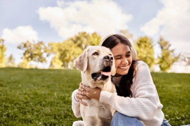 Sıcak sonbahar kıyafetlerine bürünmüş genç bir kadın parkta dinlenirken köpeğini kucaklıyor..