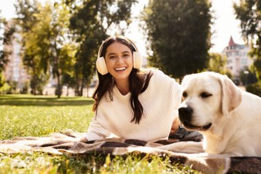 A cheerful woman in cozy autumn clothing relaxes outdoors with her dog, soaking up the sun. clipart