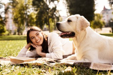 Genç bir kadın parktaki bir battaniyeye uzanıp köpeğiyle sıcak sonbahar gününün tadını çıkarıyor..