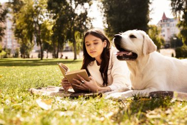 Genç bir kadın parkta kitap okuyarak huzurlu bir gün geçiriyor. Yanında da sıcak bir köpek ve battaniyesi var..