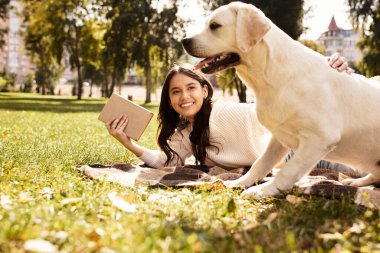 Güzel bir parkta, genç bir kadın, köpeği merakla izlerken, bir battaniyeye uzanıp kitap okuyor..