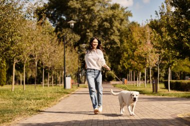 Genç bir kadın, neşeli köpeğiyle güzel bir sonbahar parkında keyifli bir yürüyüş yapıyor..