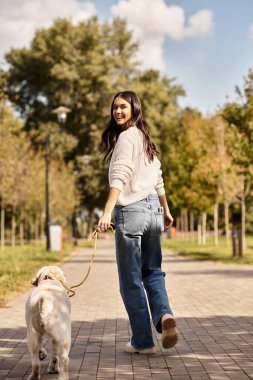 Samimi bir sonbahar elbisesi giymiş neşeli bir kadın parkta yürüyor, köpeklerinin tasmasını tutuyor..