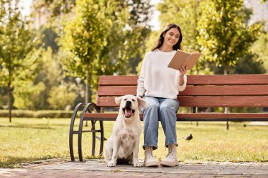 Altın yapraklar dökülürken, genç bir kadın bir bankta oturuyor, yanında köpeği ile birlikte..