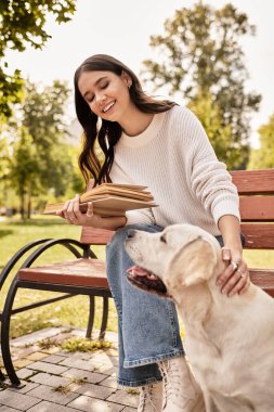 Genç bir kadın güzel bir sonbahar parkında köpeğiyle bir bankta oturup kitap okuyor..