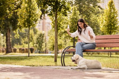 Genç bir kadın güneşli bir günün tadını çıkarıyor, köpeğiyle yemyeşil bir parkta anılarını yakalıyor..