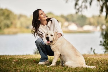 Samimi sonbahar kıyafetleri içindeki bir kadın parkta köpeğiyle oynarken sıcacık gülümsüyor..