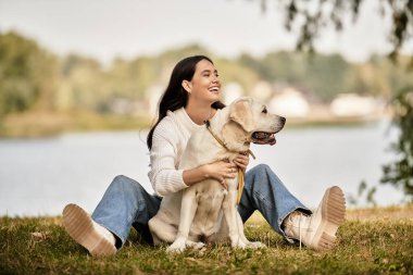 Samimi bir sonbahar elbisesi giymiş genç bir kadın köpeğiyle çimenlerde oturuyor, neşeyle gülümsüyor..