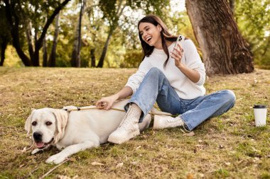 Sıcak giyimli neşeli bir kadın güzel bir sonbahar öğleden sonrasında köpeğiyle hafif bir anı paylaşır..