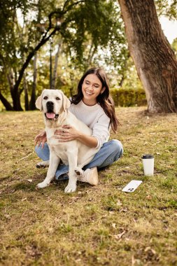 Sıcak sonbahar kıyafetleri içinde neşeli bir kadın dışarıda dinlenirken mutlu köpeğini kucaklıyor..