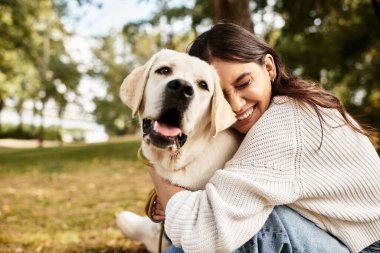 Sonbahar kıyafeti giyen genç bir kadın parkta Golden Retriever 'ıyla samimi bir anı paylaşıyor..