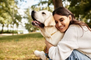 Parkta, genç bir kadın, güz yaprakları arasında köpeğiyle iç açıcı bir anın tadını çıkarıyor..