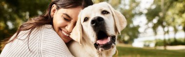 Genç bir kadın, güz parkında neşeli köpeğiyle eğlenceli bir bağ kuruyor..