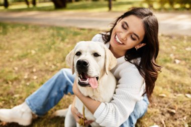 Sıcak sonbahar kıyafetleri içinde genç bir kadın güneşli bir parkta köpeğiyle neşeli bir anı paylaşıyor..
