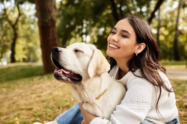 Genç bir kadın, parkta huzurlu bir sonbahar gününün tadını çıkarırken köpeğini sıcak bir şekilde kucaklıyor..