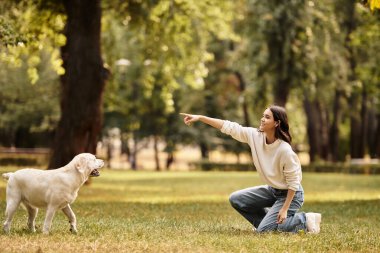 Sıcak sonbahar kıyafetleri içinde güzel bir kadın canlı bir parkta diz çöküp köpeğiyle neşeyle etkileşime girer..