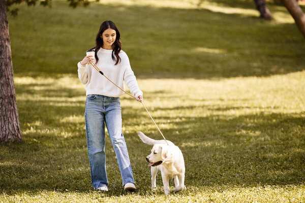 A young woman dressed in cozy autumn attire strolls happily with her dog in the park.