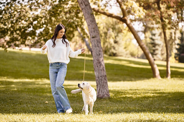 A young woman in autumn clothes walks her dog in a colorful fall park.