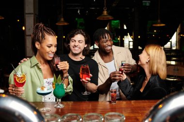 Excited coworkers toast with colorful cocktails while enjoying a joyful atmosphere together. clipart