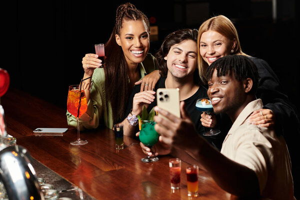 Четыре разноплановых коллеги наслаждаются напитками и смехом, запечатлевая радостный момент вместе.
