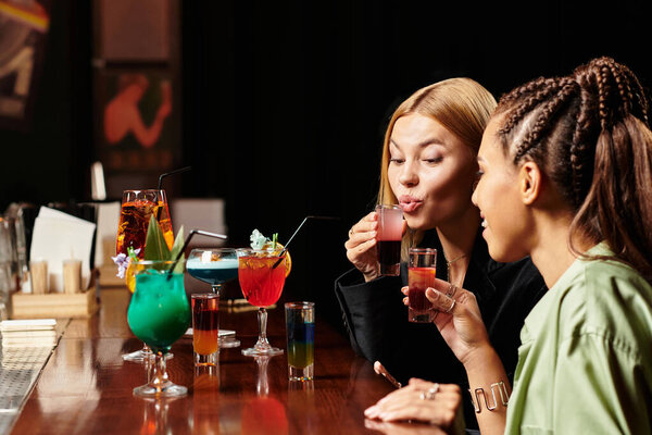 Молодые коллеги смеются и потягивают яркие коктейли, празднуя командную работу и разнообразие на мероприятии.