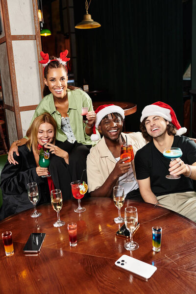 Four colleagues toast the holidays with colorful cocktails at a festive gathering.