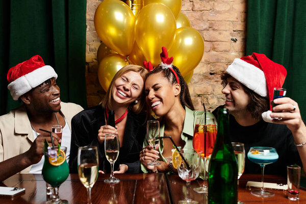 Colleagues celebrate with laughter, festive drinks, and holiday hats.