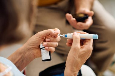 A supportive wife assists her husband as he prepares his diabetes medication at home. clipart