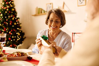 A happy senior couple enjoys the warmth of Christmas, exchanging gifts and happiness at home. clipart