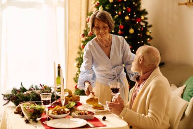 Neşeli bir son sınıf çifti dekorasyonlarla dolu sıcak bir evde keyifli bir Noel yemeğini paylaşıyor..